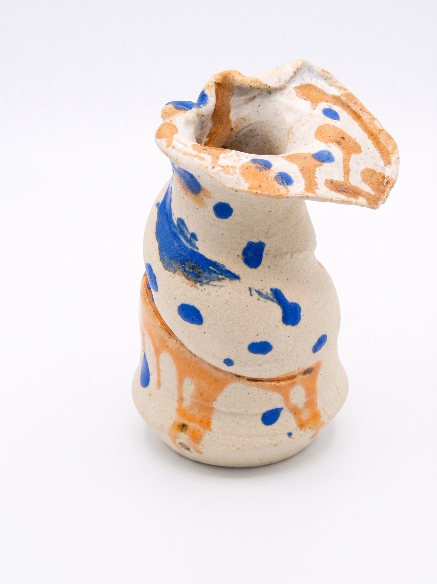 A pinched and folded bottle in raw cream stoneware, scattered with cobalt blue dots and an iron-orange band running diagonally.