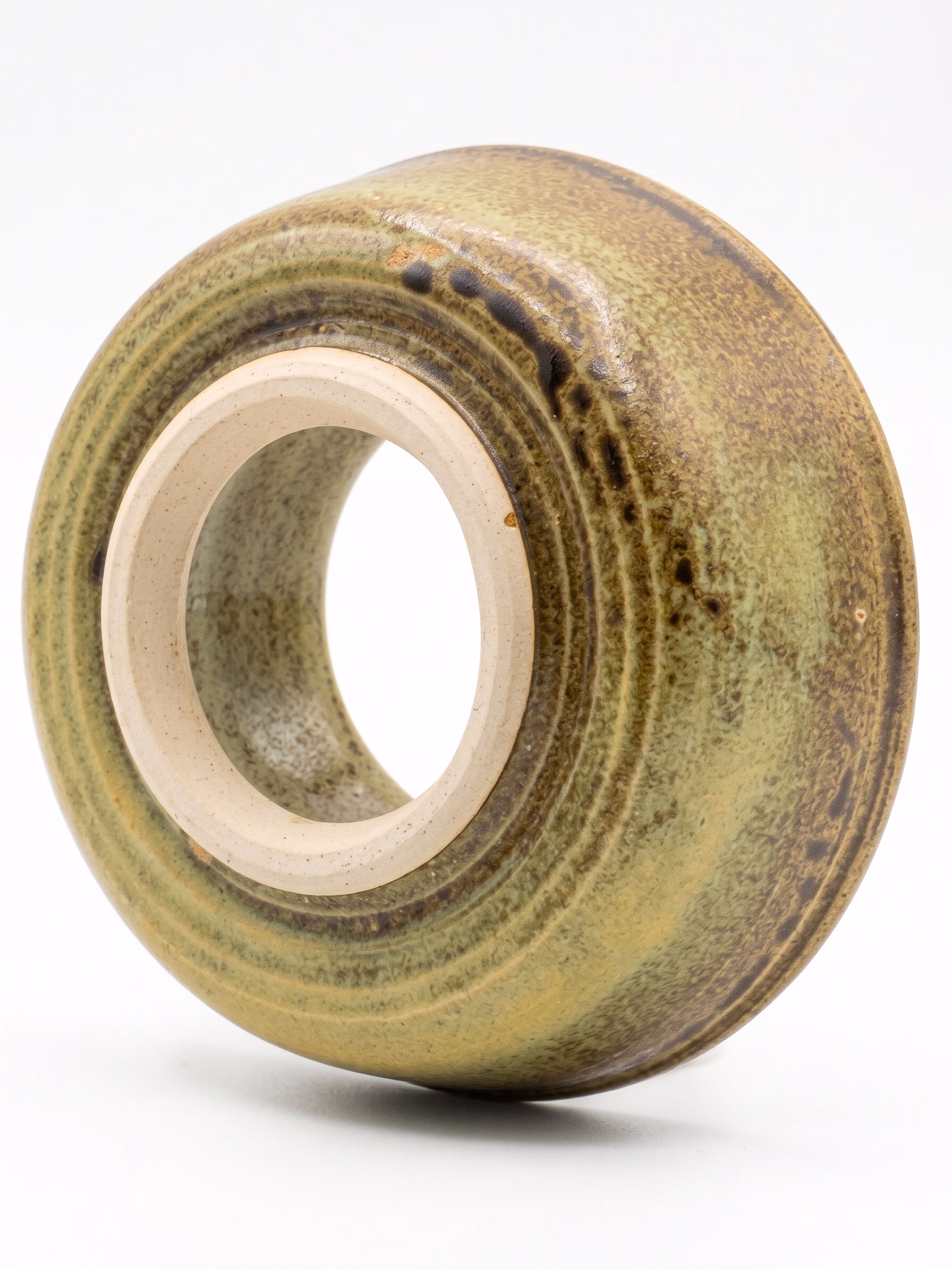 A round, doughnut-form ceramic sculpture with olive-green ash glaze and dark iron streaks.