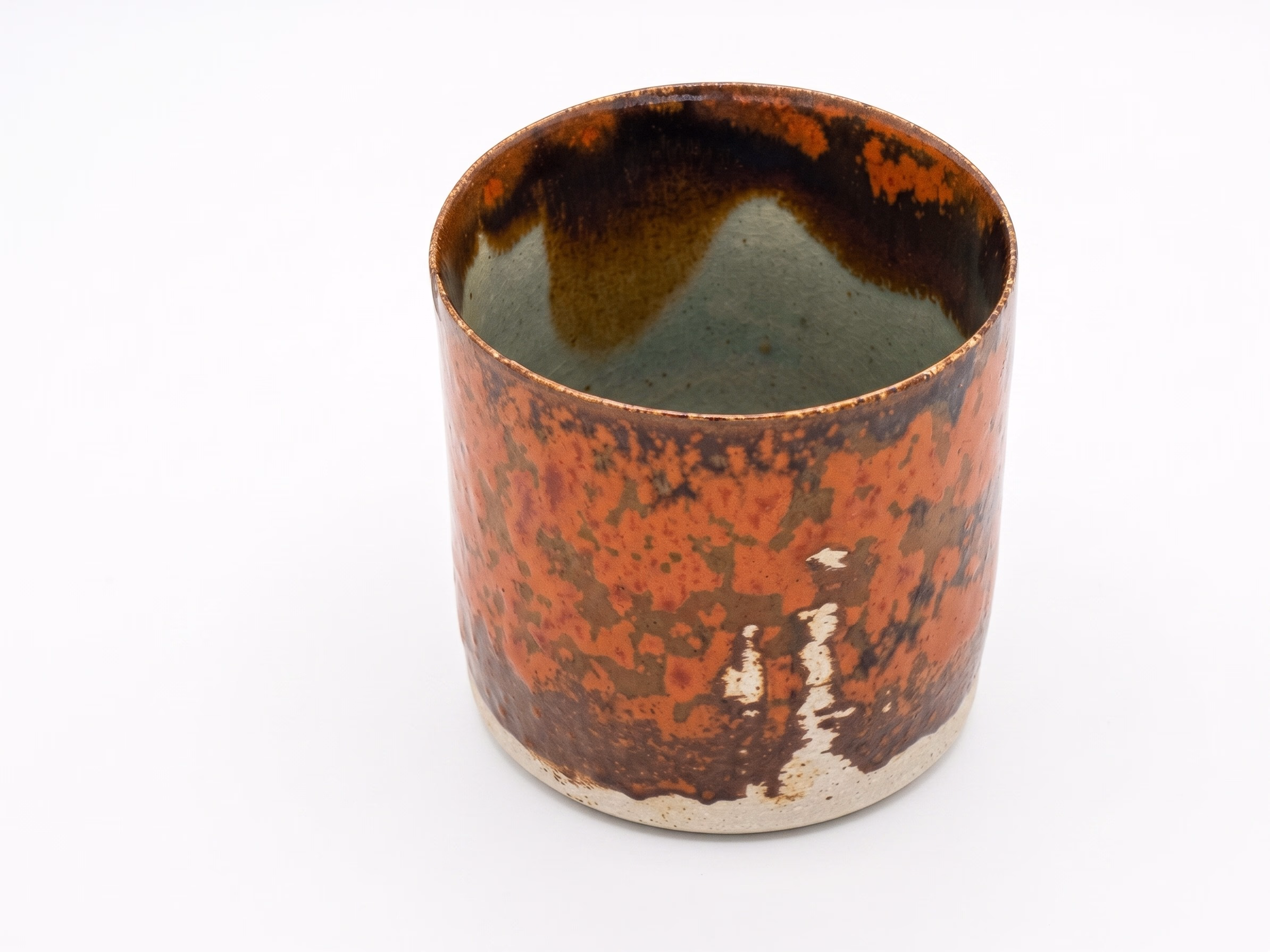A short cylindrical vessel with mottled orange-rust iron glaze on the exterior and a softer green-grey interior.