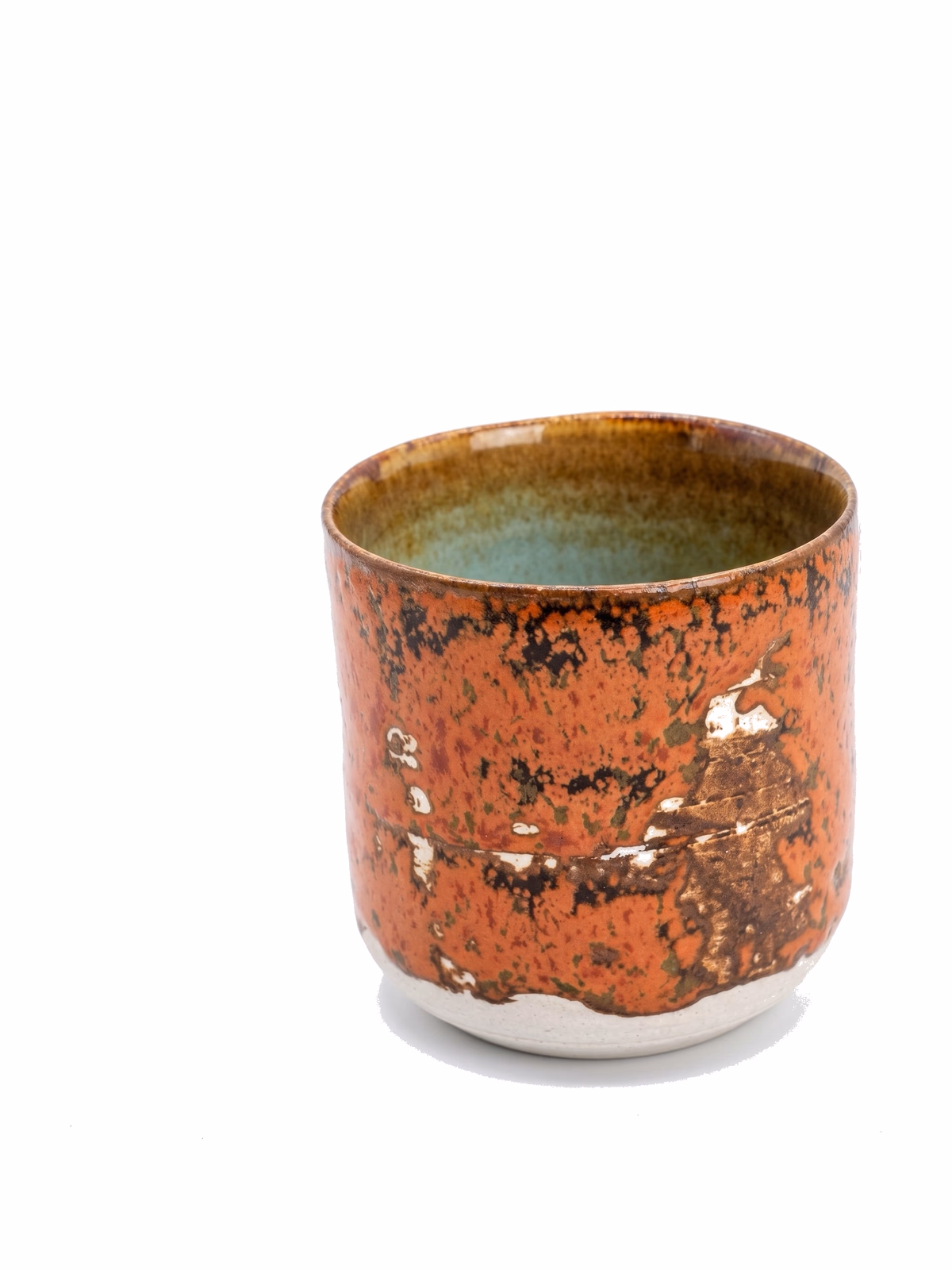 A cup in a heavily weathered iron-orange glaze with raw clay and pale revealed patches breaking through, soft green-grey interior.