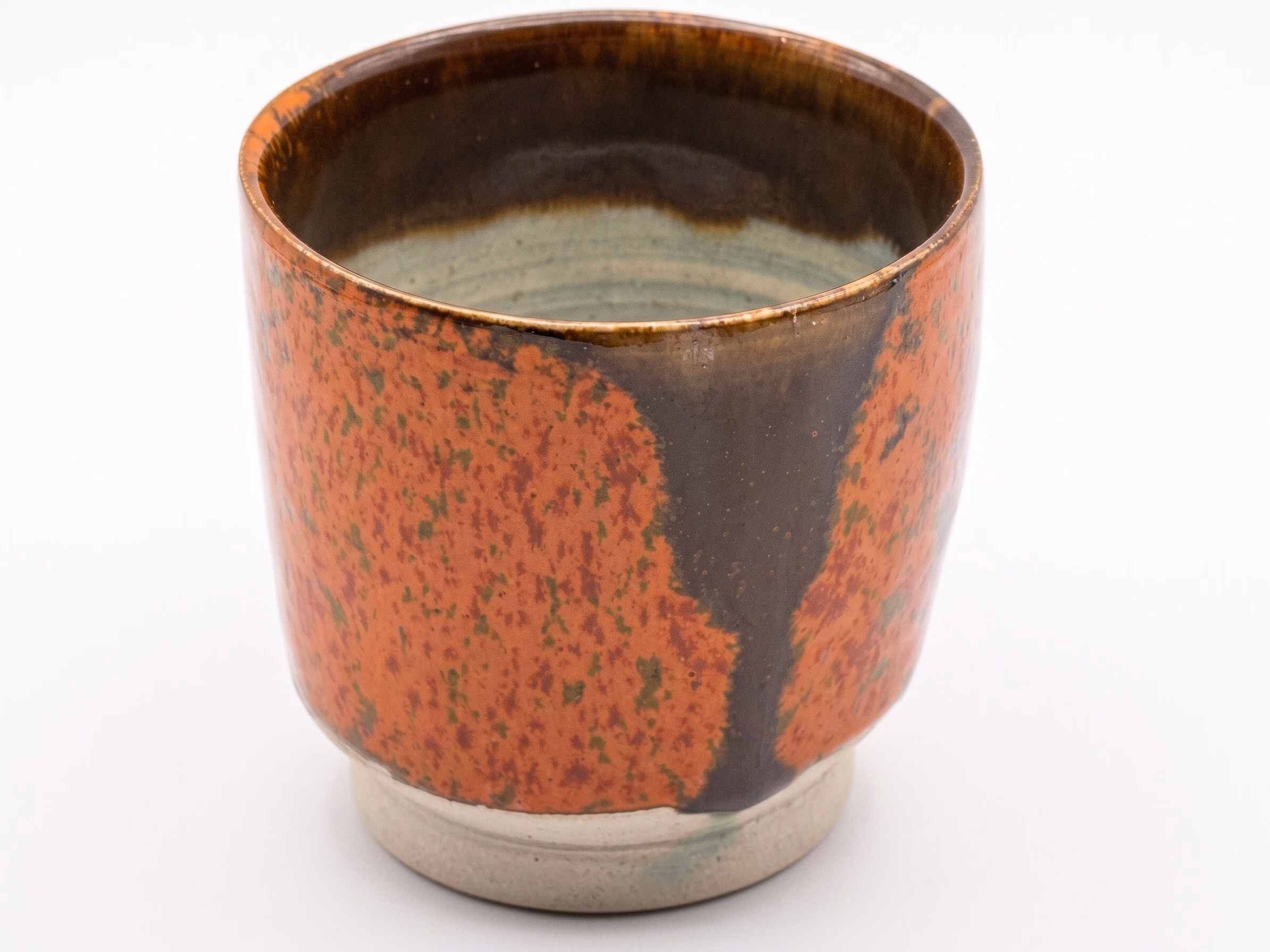 A short cup with a vivid iron-red glaze broken by a vertical dark stripe, on a raw stoneware foot.