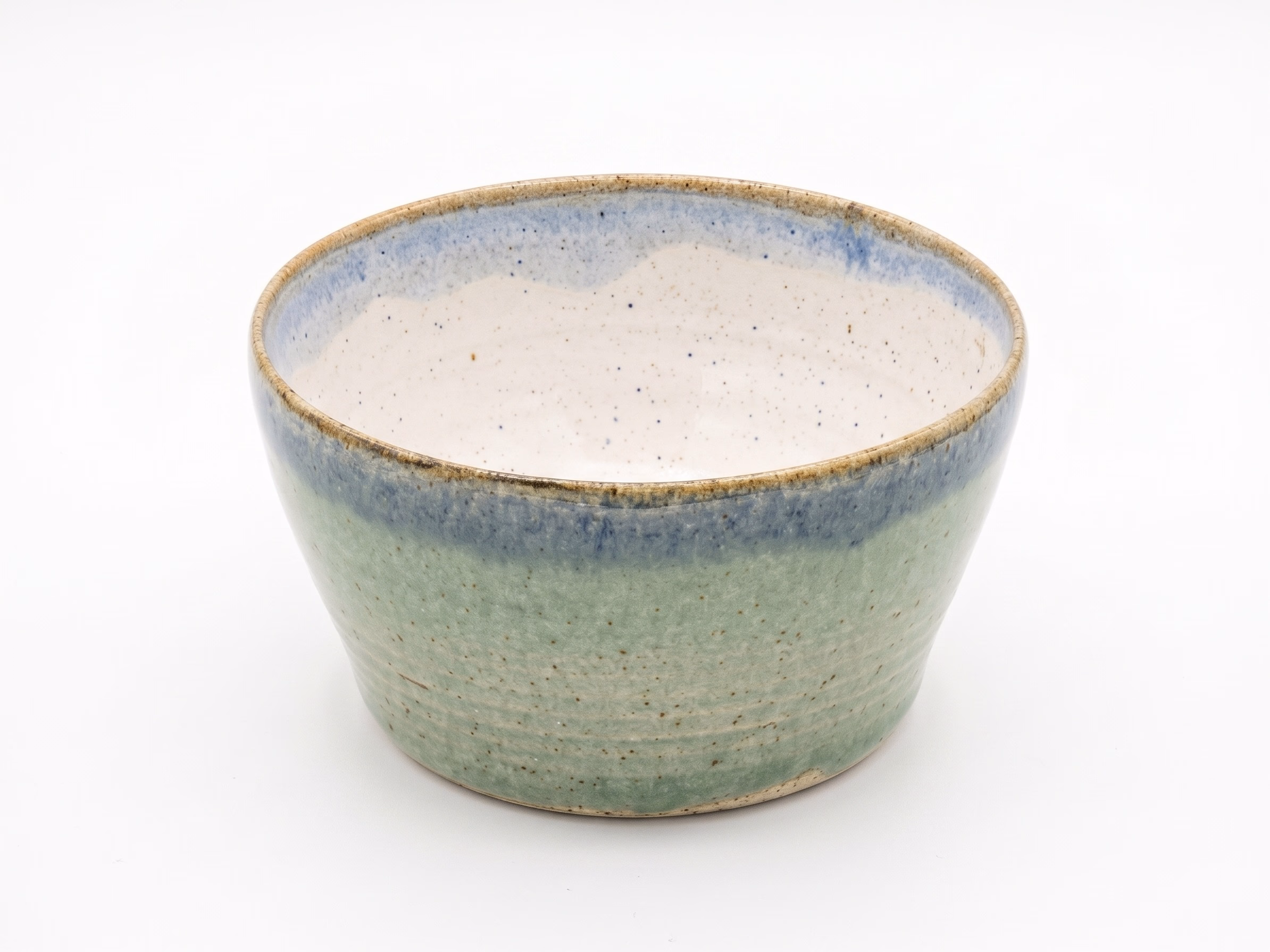 A flared bowl with a soft jade-green exterior, a cobalt blue band at the lip, and a cream speckled interior.