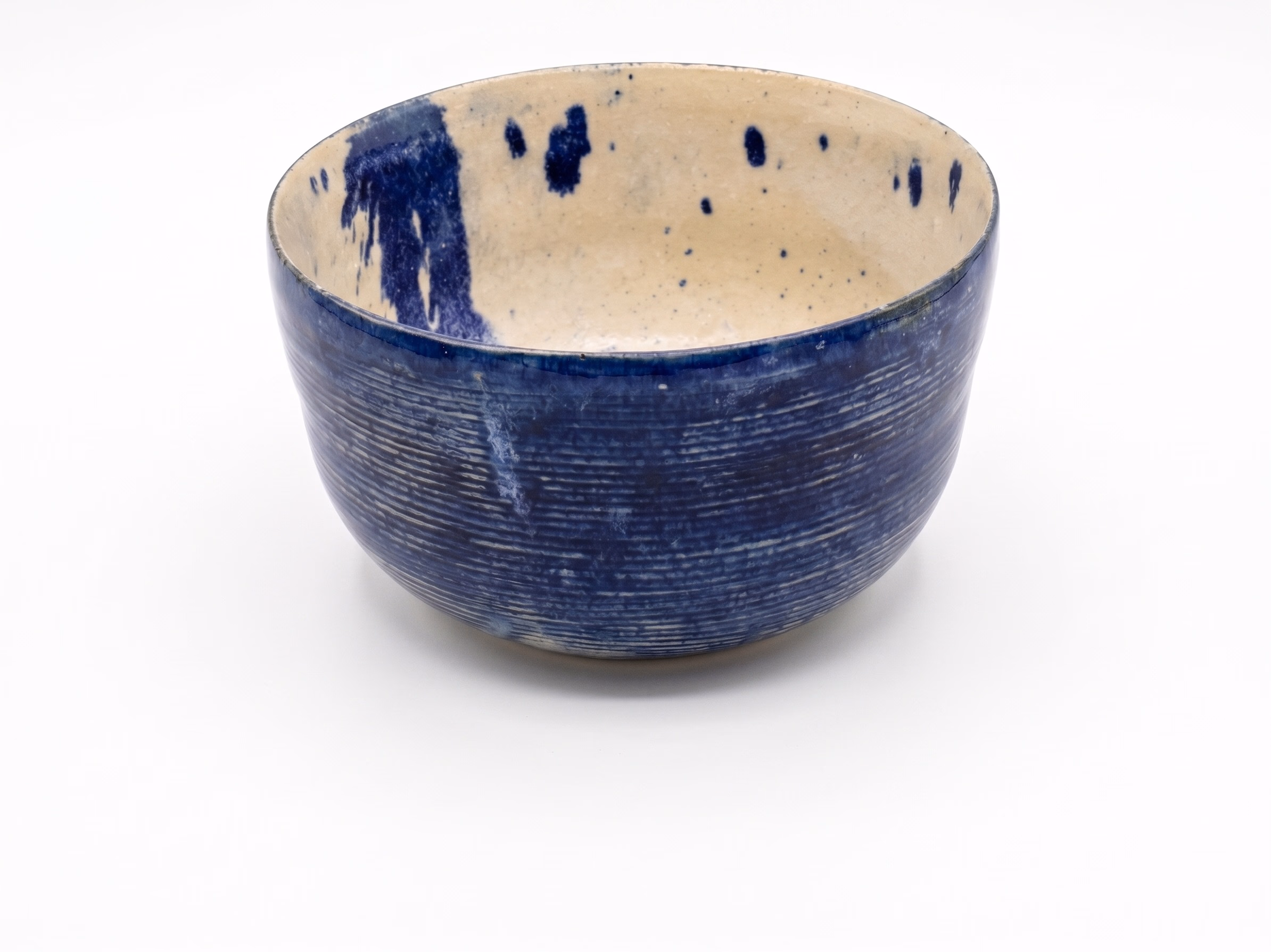 A deep ribbed stoneware bowl with cobalt-blue exterior and cream interior dripped through with navy.