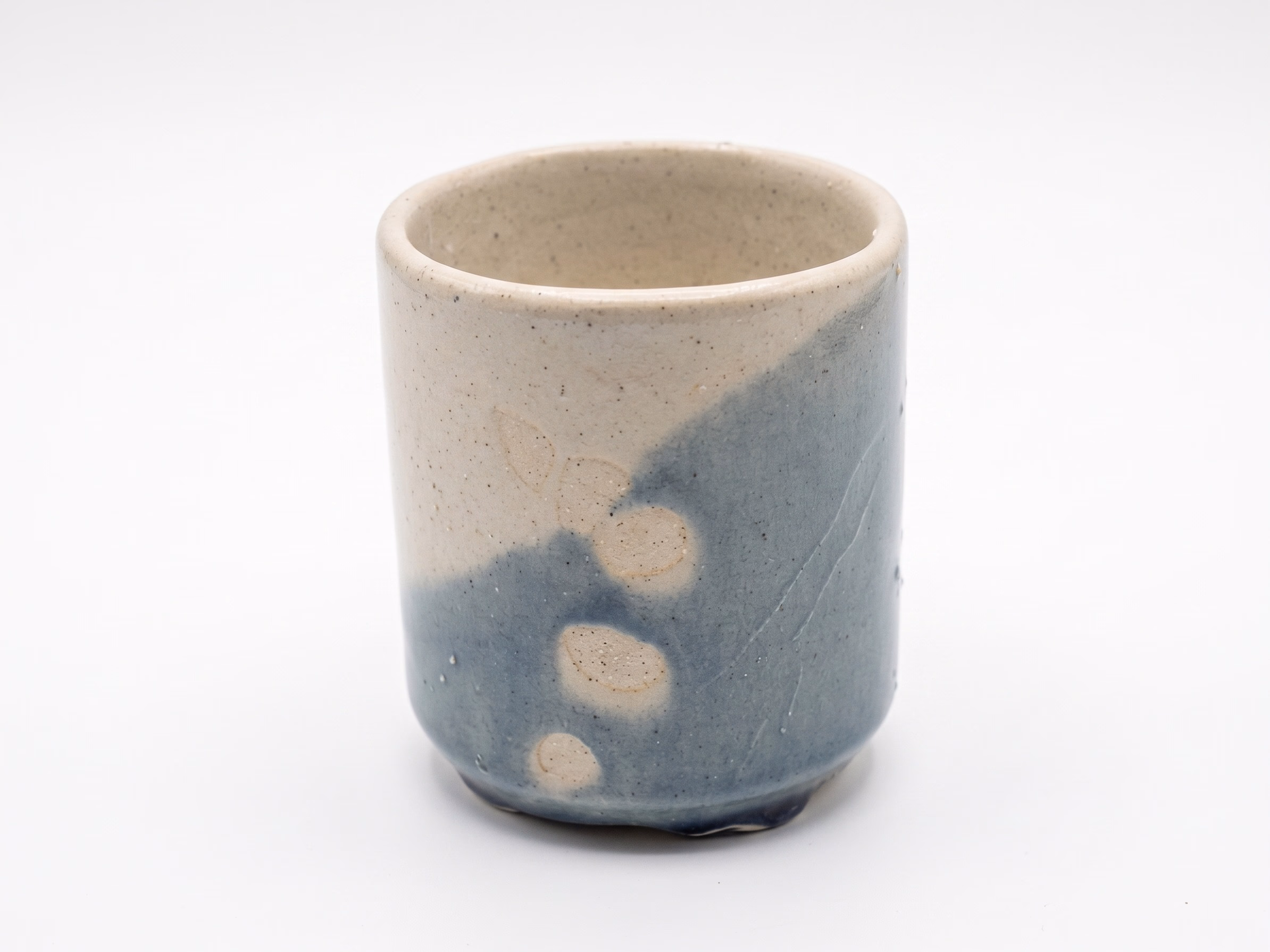 A small straight-sided cup, half cream and half slate-blue, with circular wax-resist marks where the glaze beads away.