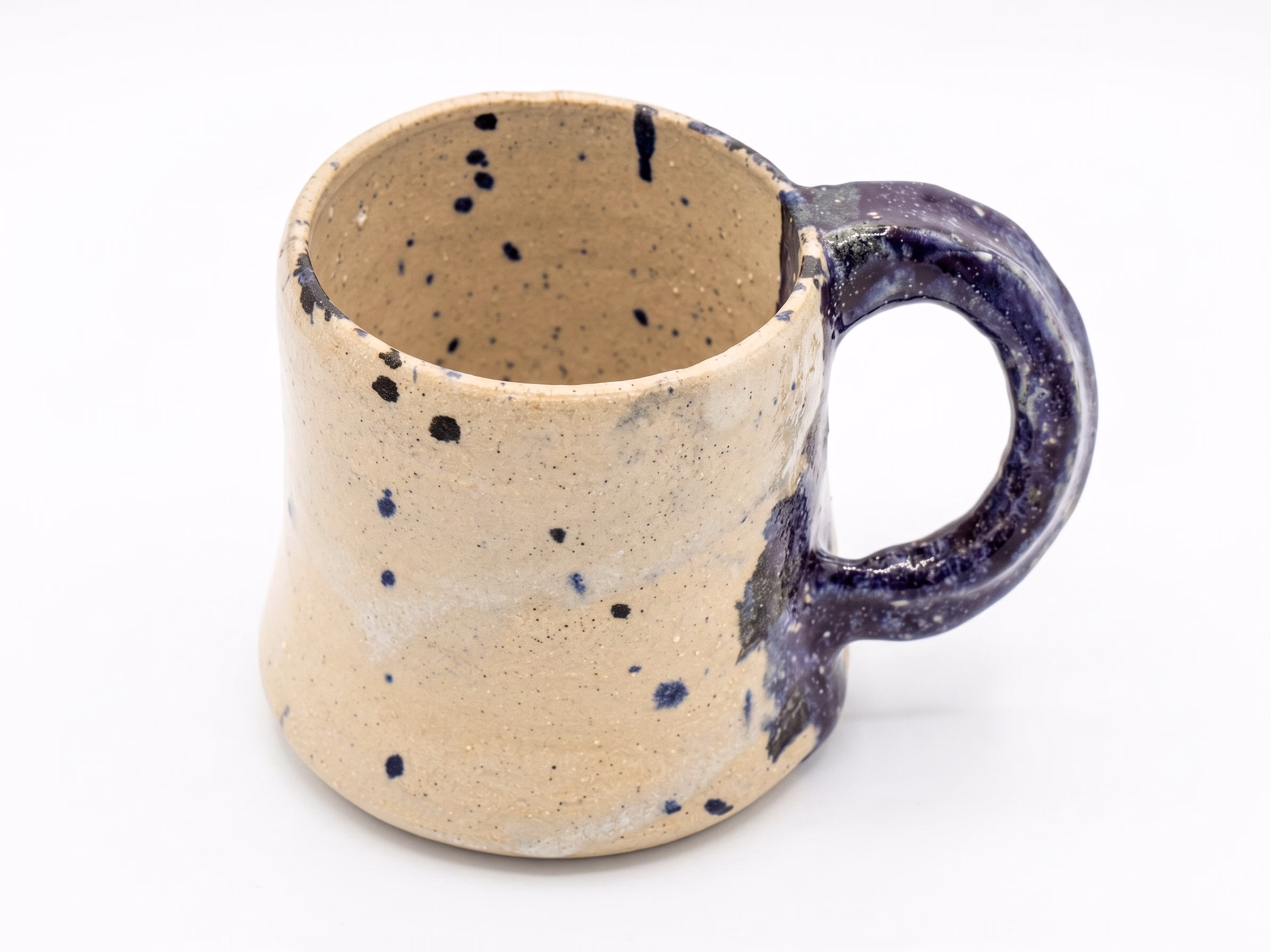 A cream stoneware mug speckled with navy, with a deep purple looped handle.